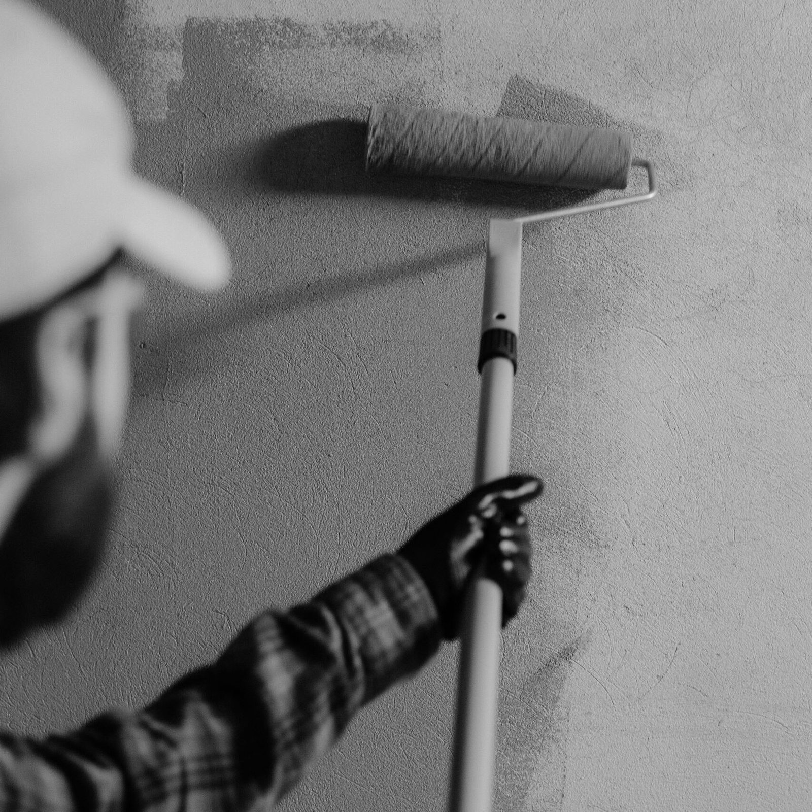 Black and white image of a painter using a roller on an interior wall.